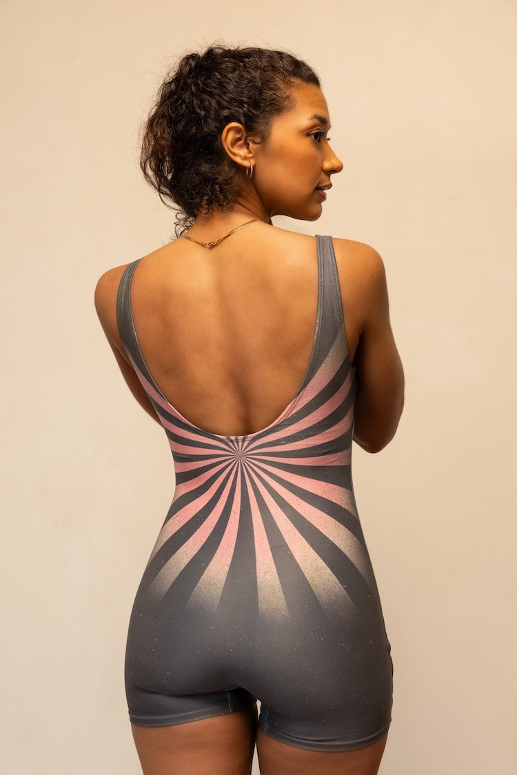 Woman wearing a gray and pink sunburst patterned bodysuit against a beige background