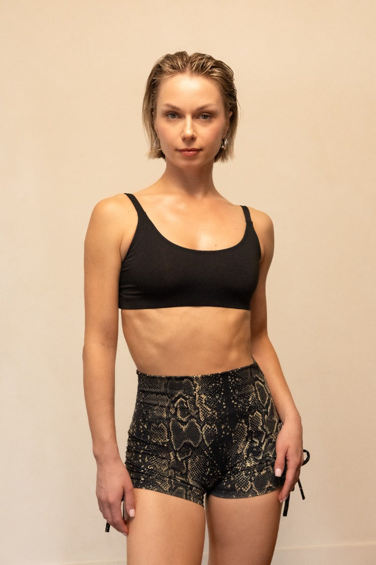 Woman wearing a black sports bra and patterned shorts on a beige background