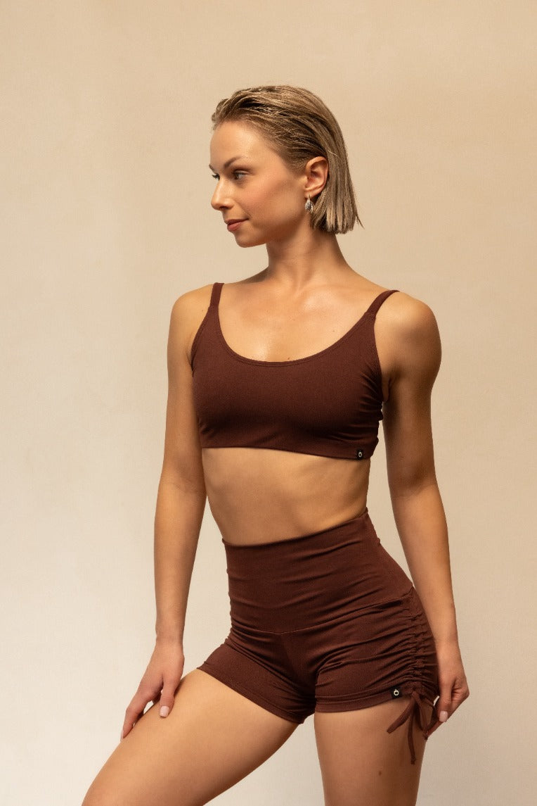 Woman wearing a brown sports bra and shorts set on a beige background