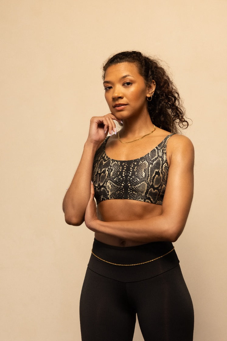 Woman wearing a patterned sports bra and black leggings against a beige background