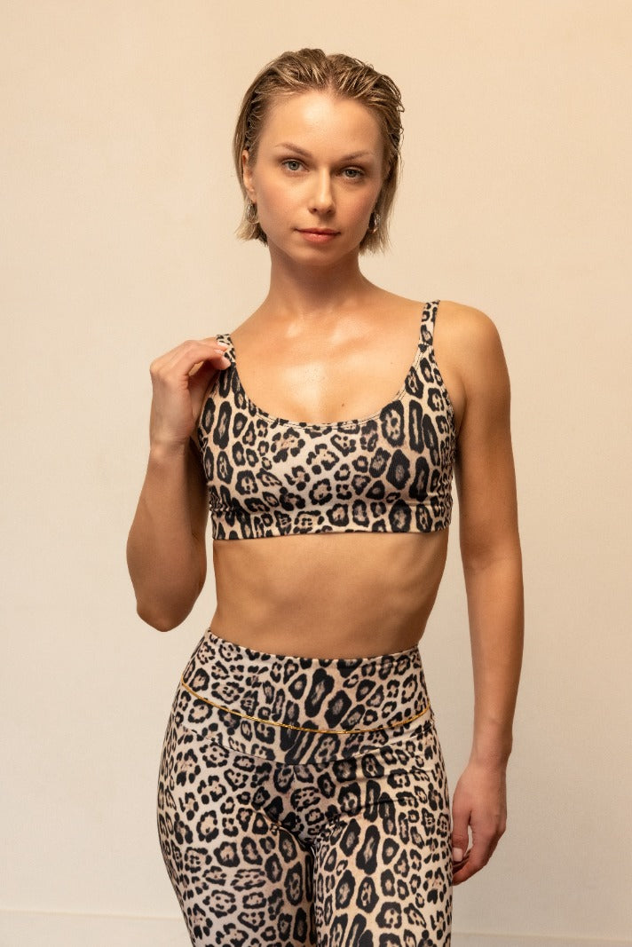Woman wearing a leopard print sports bra and leggings against a beige background