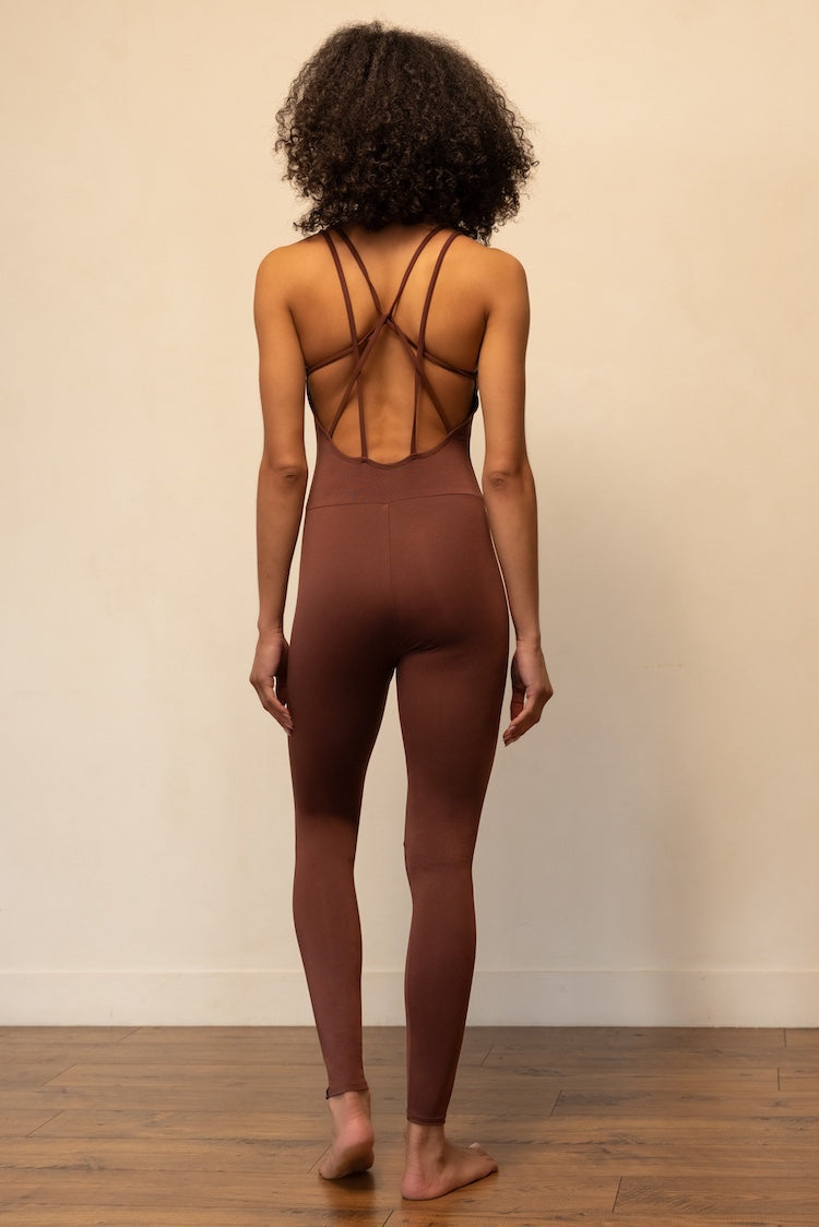 Person wearing a brown bodysuit with open back against a beige wall.