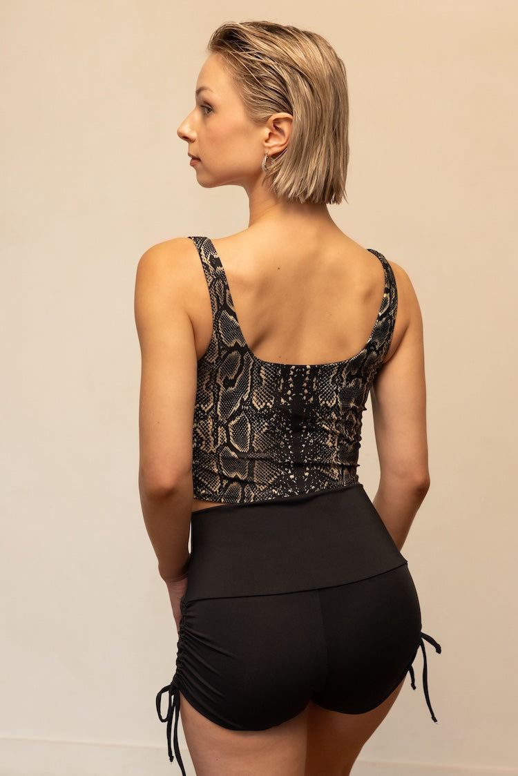 Woman wearing a black snake print top and black shorts on a beige background