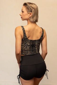 Woman wearing a black snake print top and black shorts on a beige background
