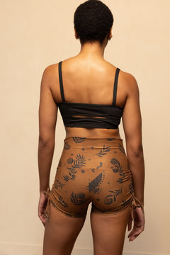 Person wearing a black crop top and brown shorts with floral patterns on a beige background