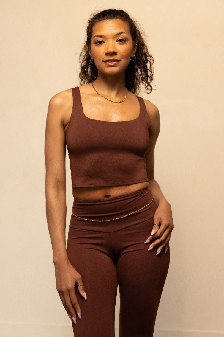 Woman wearing a brown tank top and leggings against a beige background