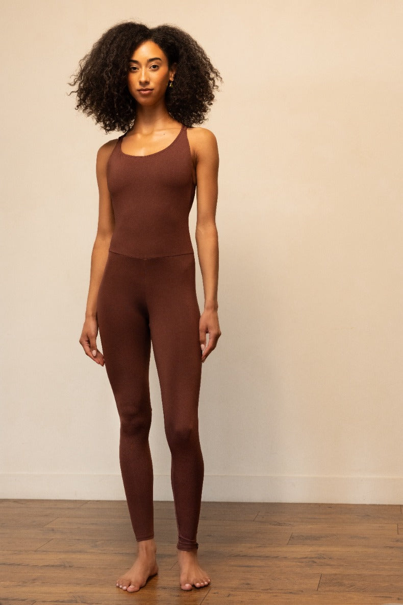 Woman wearing a brown tank top and leggings against a plain background